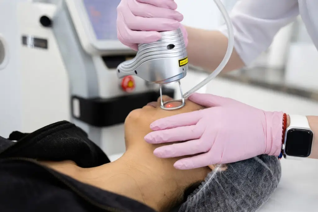 Medical professional in pink gloves performing laser treatment on a patient’s neck.